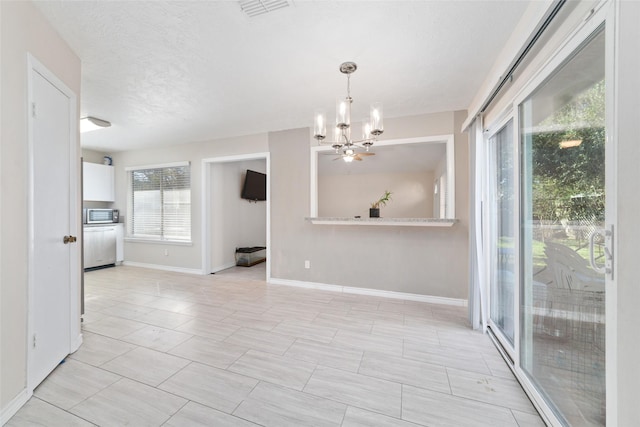 empty room featuring a wealth of natural light, a chandelier, and a textured ceiling