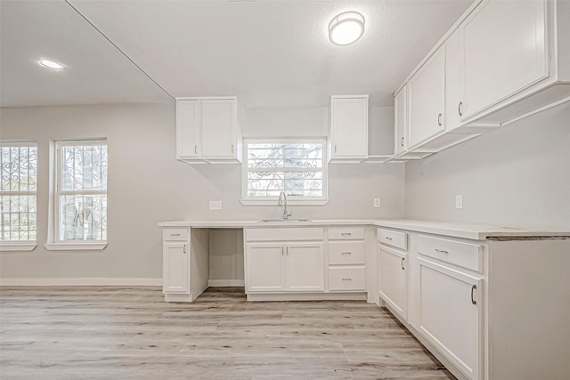 kitchen with light wood-type flooring, white cabinetry, and sink