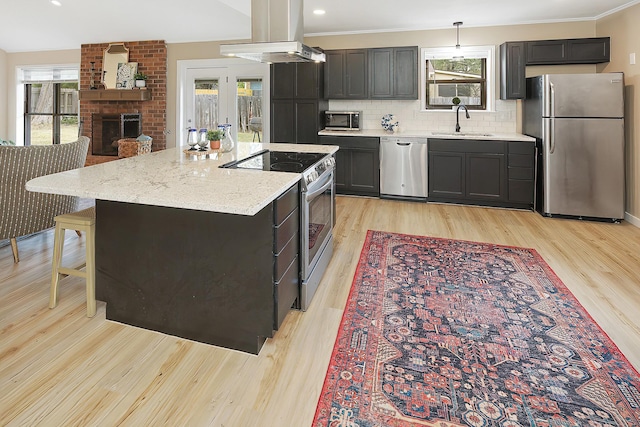 kitchen featuring island exhaust hood, appliances with stainless steel finishes, tasteful backsplash, a brick fireplace, and sink