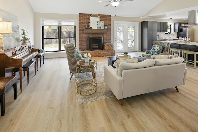 living room with ceiling fan, light hardwood / wood-style floors, a fireplace, and vaulted ceiling