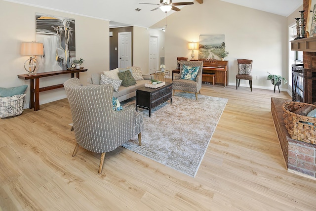 living room featuring lofted ceiling with beams, light hardwood / wood-style floors, a brick fireplace, and ceiling fan