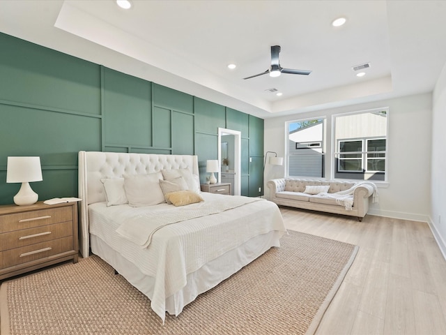 bedroom with ceiling fan, a raised ceiling, and light wood-type flooring