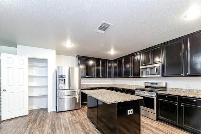 kitchen with light stone countertops, appliances with stainless steel finishes, light hardwood / wood-style flooring, and a kitchen island