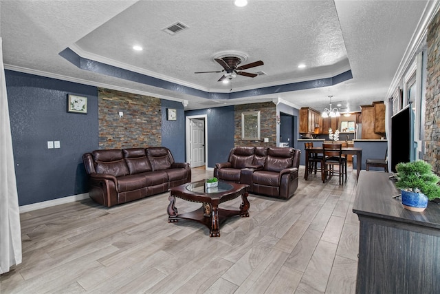 living room featuring ceiling fan with notable chandelier, ornamental molding, a textured ceiling, and a tray ceiling