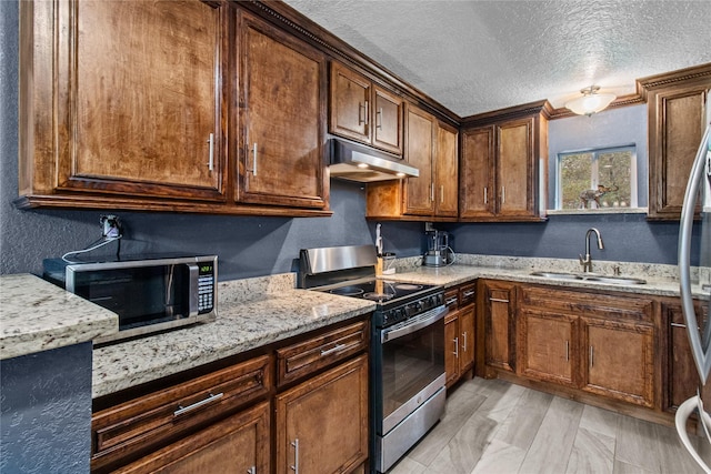 kitchen featuring light stone countertops, a textured ceiling, stainless steel appliances, and sink