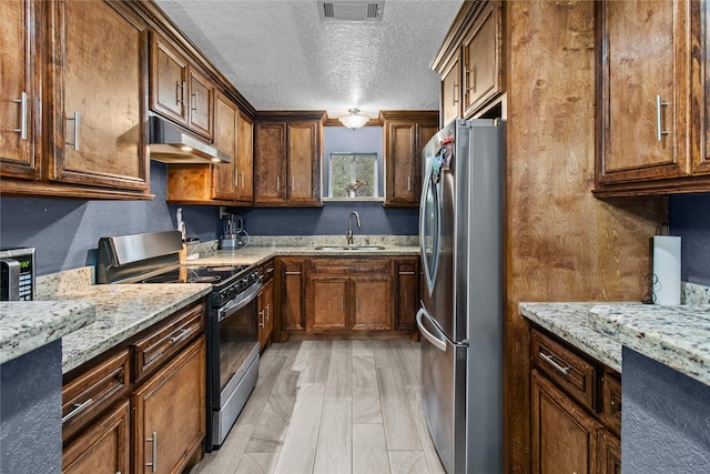 kitchen with sink, light hardwood / wood-style flooring, a textured ceiling, light stone counters, and stainless steel appliances