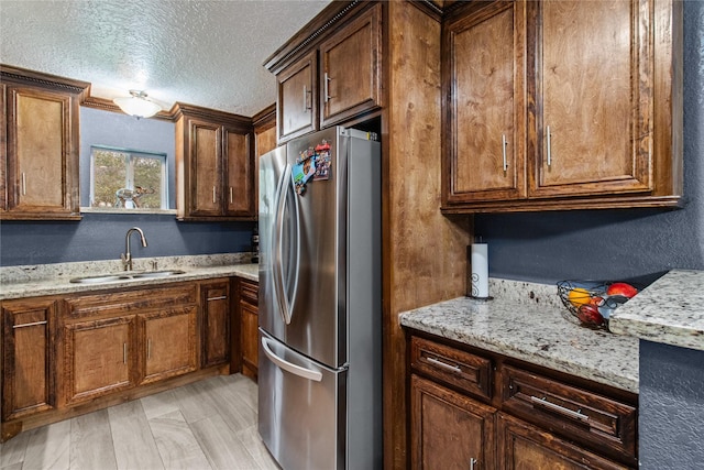 kitchen with light stone countertops, stainless steel fridge, light wood-type flooring, a textured ceiling, and sink