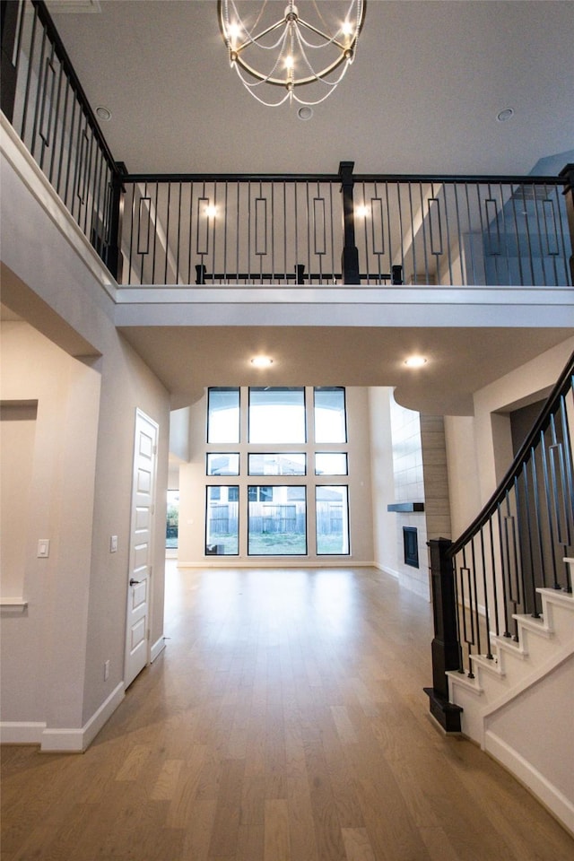 foyer entrance featuring a tiled fireplace, a towering ceiling, wood-type flooring, and an inviting chandelier