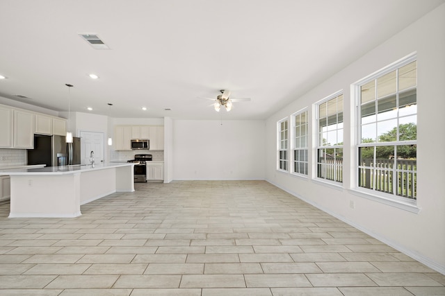 interior space featuring white cabinetry, a kitchen island with sink, decorative light fixtures, decorative backsplash, and appliances with stainless steel finishes