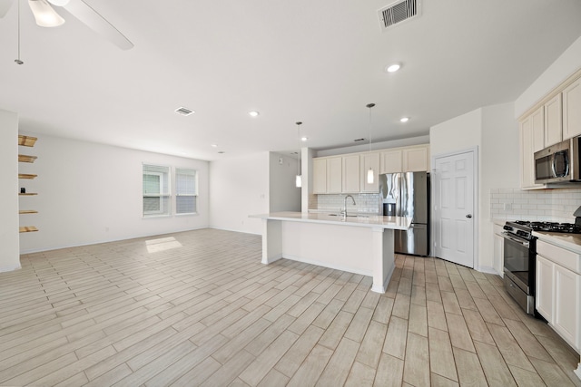 kitchen with decorative backsplash, a kitchen island with sink, hanging light fixtures, and stainless steel appliances