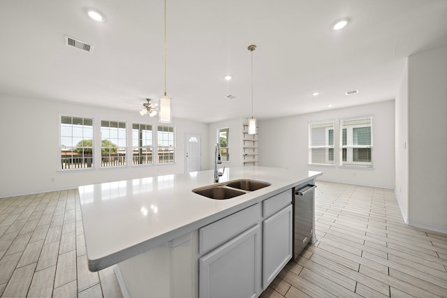 kitchen with ceiling fan, sink, hanging light fixtures, and an island with sink