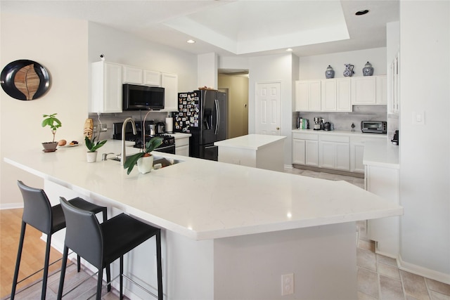 kitchen with a breakfast bar area, a peninsula, decorative backsplash, black appliances, and a center island