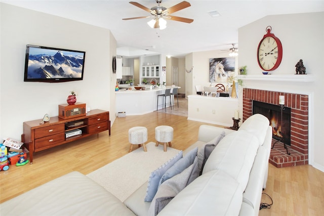 living room with a brick fireplace, light hardwood / wood-style flooring, and ceiling fan