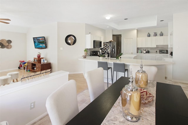 tiled dining area featuring a raised ceiling and ceiling fan