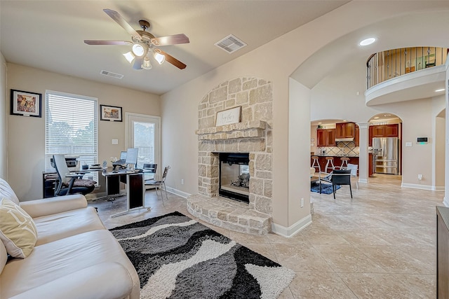 tiled living room with a stone fireplace and ceiling fan