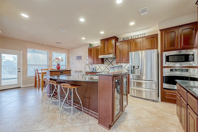 kitchen featuring sink, stainless steel appliances, dark stone counters, a breakfast bar area, and a center island with sink