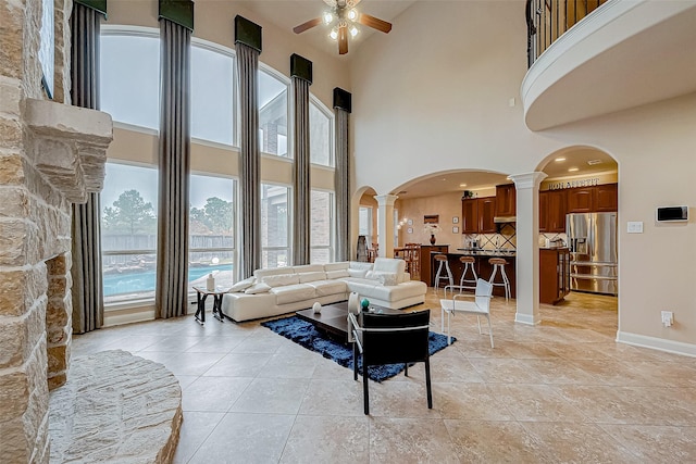 living room featuring ceiling fan, a towering ceiling, light tile patterned floors, and decorative columns