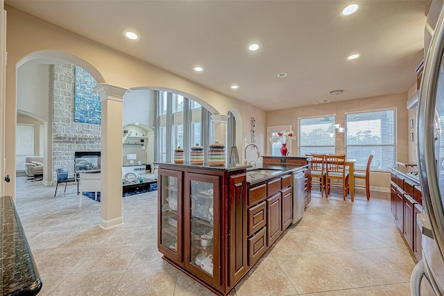 kitchen featuring sink, a stone fireplace, stainless steel dishwasher, dark stone counters, and decorative light fixtures