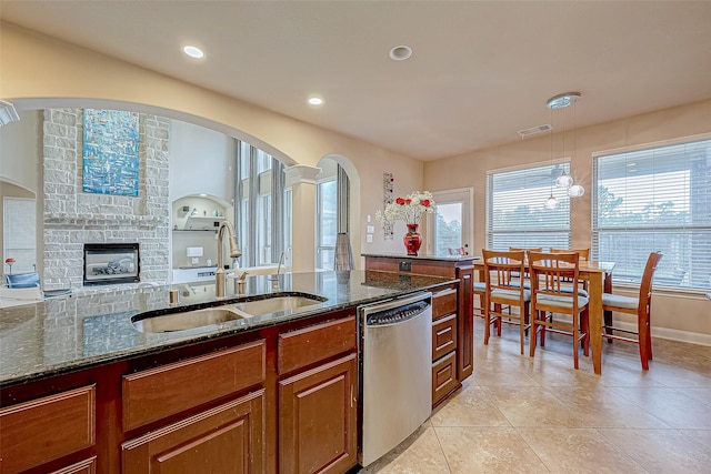 kitchen featuring sink, a multi sided fireplace, stainless steel dishwasher, dark stone counters, and pendant lighting