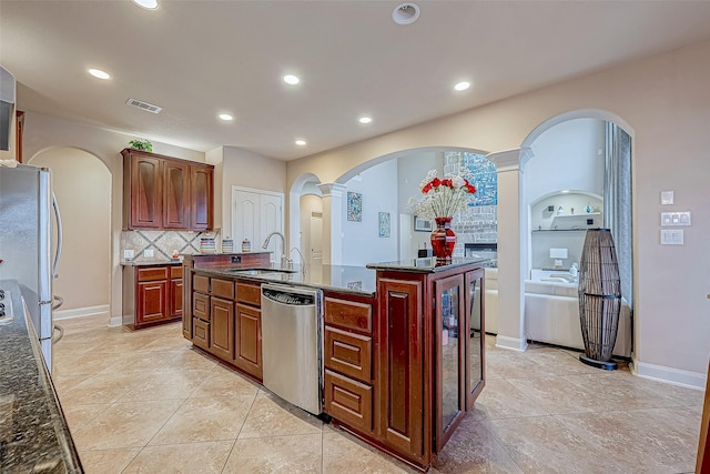 kitchen featuring appliances with stainless steel finishes, decorative columns, tasteful backsplash, a kitchen island with sink, and sink