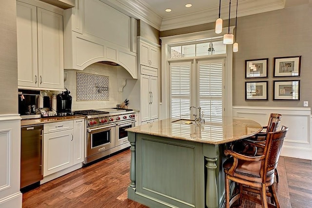 kitchen featuring backsplash, hanging light fixtures, a kitchen island with sink, range with two ovens, and light stone counters