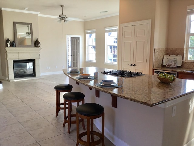 kitchen with black gas stovetop, a kitchen bar, stone countertops, ceiling fan, and light tile patterned floors