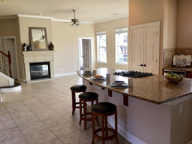 kitchen featuring black gas stovetop, ceiling fan, dark stone countertops, a breakfast bar, and light tile patterned floors