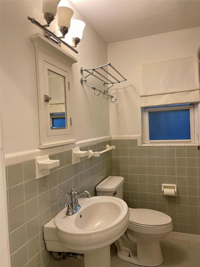 bathroom with toilet, tile patterned floors, tile walls, and sink