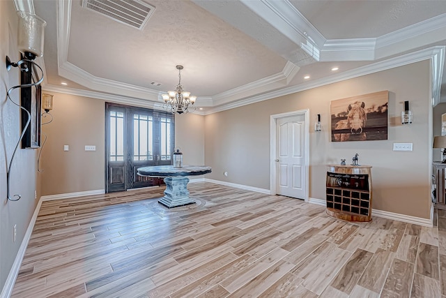 interior space with light wood-type flooring, ornamental molding, a tray ceiling, and a chandelier