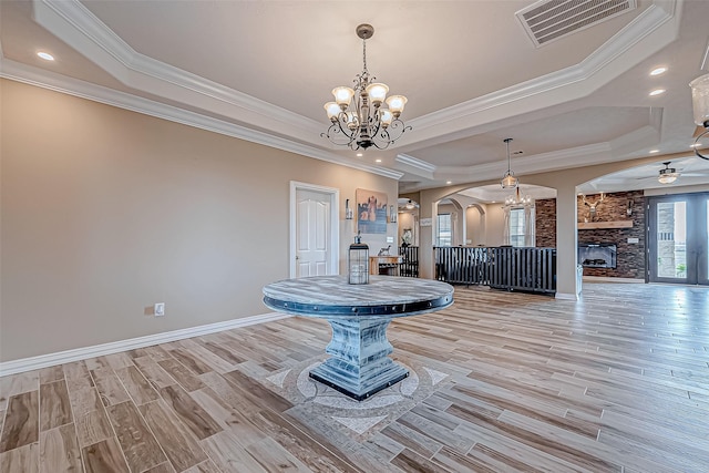 unfurnished dining area featuring a tray ceiling, a stone fireplace, crown molding, and light hardwood / wood-style flooring