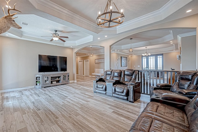 living room featuring a raised ceiling, light hardwood / wood-style flooring, ceiling fan with notable chandelier, and ornamental molding