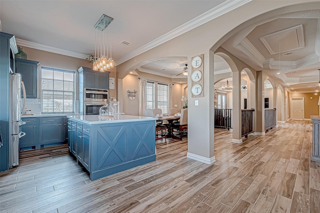 kitchen featuring ceiling fan with notable chandelier, light hardwood / wood-style flooring, ornamental molding, an island with sink, and decorative light fixtures