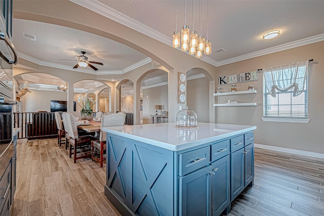 kitchen featuring blue cabinets, crown molding, decorative light fixtures, light hardwood / wood-style flooring, and a center island