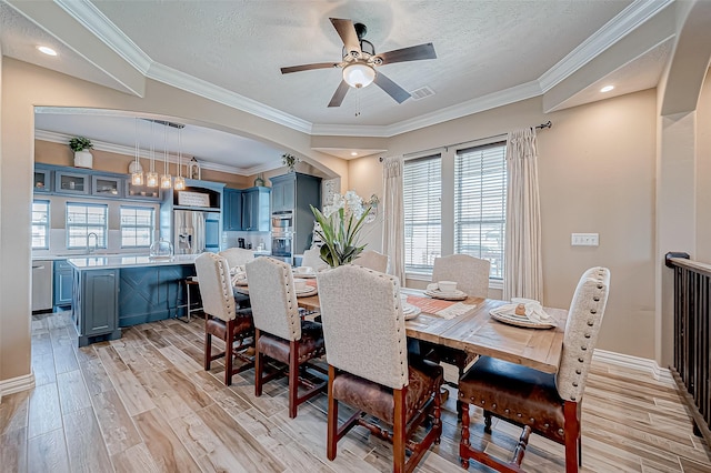 dining area featuring ceiling fan, light wood-type flooring, a textured ceiling, and ornamental molding