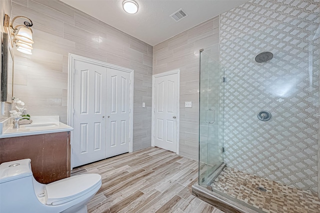 bathroom with vanity, hardwood / wood-style flooring, toilet, tile walls, and an enclosed shower