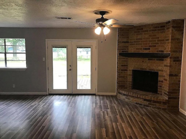 unfurnished living room featuring ceiling fan, french doors, dark wood-type flooring, a textured ceiling, and a fireplace