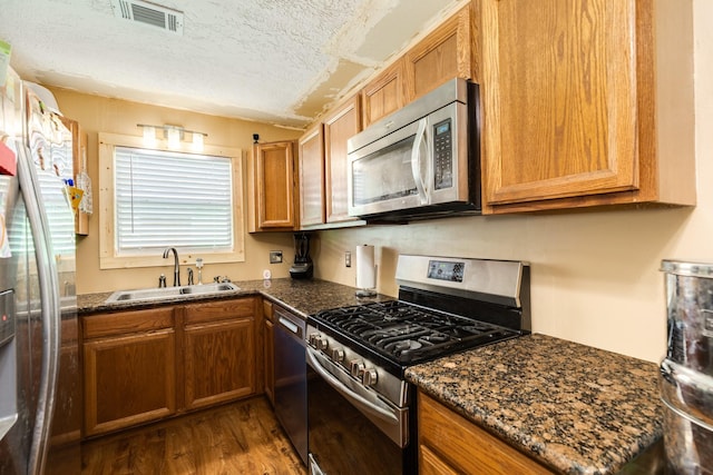 kitchen with dark hardwood / wood-style flooring, sink, stainless steel appliances, and dark stone counters