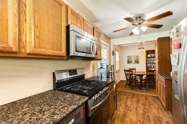 kitchen featuring hardwood / wood-style flooring, ceiling fan, dark stone countertops, and appliances with stainless steel finishes