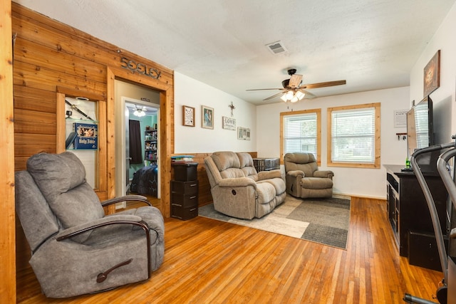 living room featuring hardwood / wood-style floors, ceiling fan, and wood walls