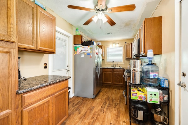 kitchen featuring stainless steel fridge, ceiling fan, sink, hardwood / wood-style flooring, and dark stone countertops