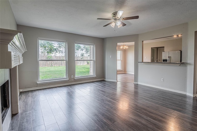 unfurnished living room with ceiling fan with notable chandelier, a textured ceiling, and dark hardwood / wood-style floors