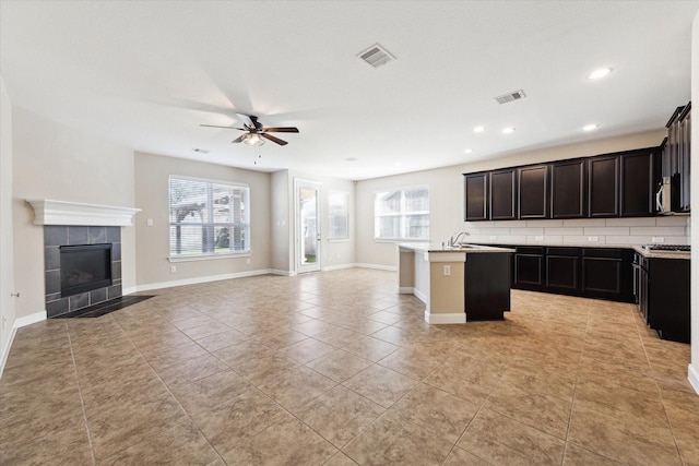 kitchen featuring ceiling fan, a kitchen island with sink, a wealth of natural light, and a tiled fireplace