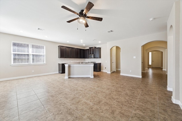 kitchen with a kitchen island with sink, decorative backsplash, ceiling fan, dark brown cabinets, and stainless steel appliances