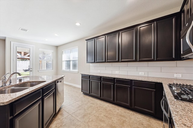 kitchen with backsplash, light stone countertops, sink, and stainless steel appliances