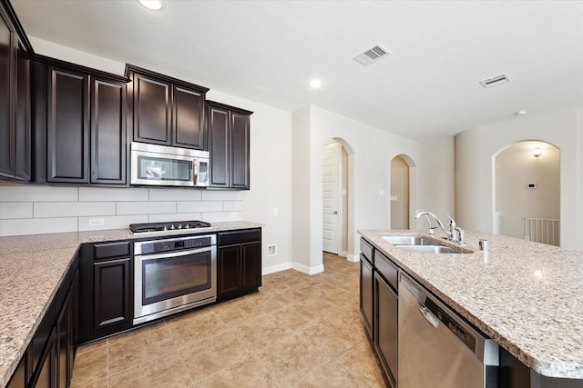 kitchen featuring a kitchen island with sink, sink, light tile patterned floors, tasteful backsplash, and stainless steel appliances