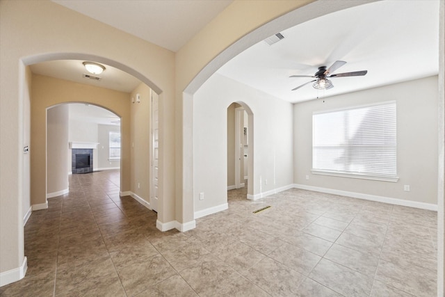 tiled empty room featuring ceiling fan and a fireplace