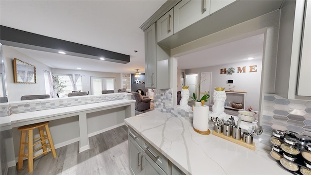 kitchen with decorative backsplash, light stone countertops, gray cabinetry, and ceiling fan