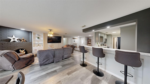 living room with ceiling fan, built in shelves, a fireplace, and light hardwood / wood-style flooring