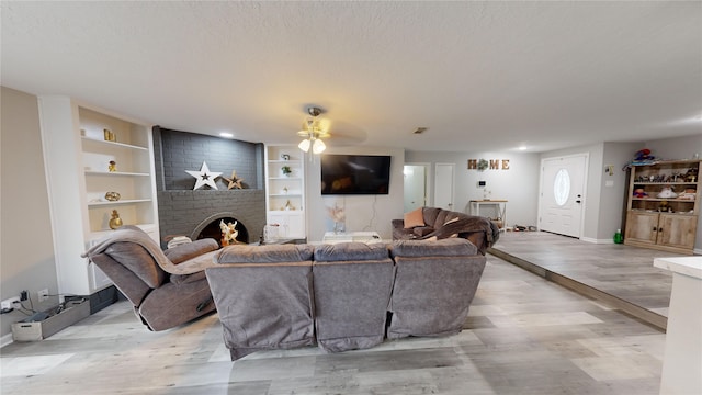 living room with ceiling fan, light hardwood / wood-style floors, a textured ceiling, and a brick fireplace