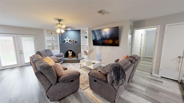 living room featuring french doors, a brick fireplace, ceiling fan, built in features, and light hardwood / wood-style floors